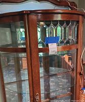 Full frontal view of oak curio cabinet showing curved glass shelves, mirrored back and leaded-glass doors