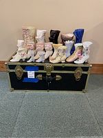Front view showing collection of 17 Victorian-style earthenware boots arranged on top of a black vintage Seward chest.