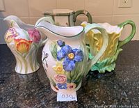 Front view of four floral ceramic pitchers on black counter showing different detailed flower designs.