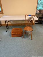Plastic folding table and wooden chair and two cushions shown together in a room on carpet