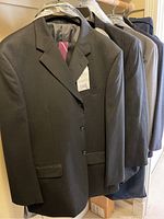 Full view of five men's suit jackets hanging on hangers, showing varying shades of gray and dark colors.
