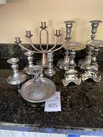 Full collection of assorted pewter and metal candelabras and candle holders arranged on granite countertop showing variety of sizes and designs.