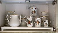 photo of Godinger and Co porcelain set with three pitchers, two saucers, and one canister, showing floral designs and gold trim