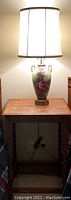 Wood table with carved legs, medium brown finish, holding a ceramic floral lamp with fabric shade