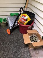 Overall lot showing garden pots, soil bags, weed wacker, box with string lights and glass float box