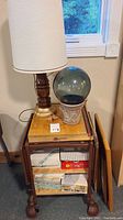 Tall vintage lamp with wooden and brass base and off-white fabric shade on top of small metal desk
