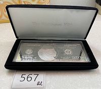 Silver-plated $100 note displayed in black presentation case with lid open showing front side