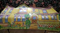 Photo of yellow doll house shaped rug with purple curtains and garden details, spread on a surface