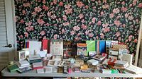 Wide view of entire lot showing diverse stationary and office supplies arrayed on table against floral wallpaper background.