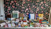 Full lot view on white table against floral wallpaper, showing all items grouped for sale including note cards, notebooks, files, writing instruments, and displays