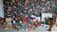 Photo showing variety of games and toys including boxed chess set, colorful wooden abacuses, numerous card and board games, crayons, puzzles, and plush toys.
