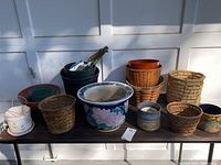 Photo of various garden pots including ceramic, plastic, and woven baskets with gardening tools on a table in natural light.