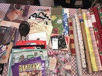 Overview of gift bags with assorted designs and multiple rolls of gift wrap paper laid out on a table.