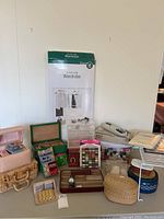 Overall view of lot showing multiple jewelry boxes of various materials and sizes, sewing items, unopened wardrobe package and clean assortment of other items including watch and stapler.