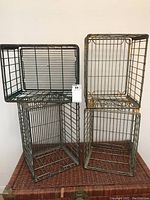 Front view showing 4 metal milk crates in different sizes stacked on a woven chest. Crates are open grid metal wire, painted in various colors with worn and chipped paint.