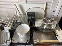 Overview of lot showing plastic punch bowl with utensils, mirrored place mats, modern black carafe in box, white trays, and metal bowl.