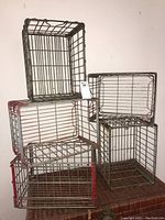 Five vintage metal milk crates stacked, showing different sizes and chipped paint.
