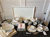Full lot arrangement on table showing plates, teapots, cups and saucers, cloth napkins, tablecloth, and napkin rings.
