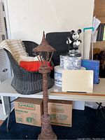 Photo showing black wicker chair, decorative hat boxes, vintage Mickey Mouse telephone, tall vine lamp post, and blue rolling hand cart on a table