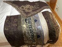 Overall view of one vintage triangular scarf and seven reversible rectangular pashminas laid out on bed, showing patterns and colors.