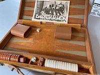 Backgammon board open showing playing surface, dice, dice cups, and playing pieces in the case with visible wear on the brown exterior.
