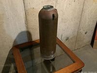 Front view of vintage copper fire extinguisher body placed on a glass-top table showing its cylindrical shape and patina.