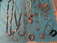 Overview of diverse costume jewelry including a variety of necklaces with beads, metal pendants, and bracelets laid out on a blue background.