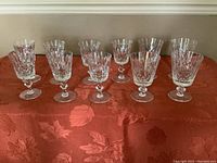 Seven white wine glasses and five red wine glasses arranged on a reddish tablecloth, showing the cut crystal Cross and Olive pattern.