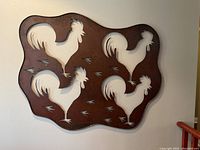 Front view of large metal wall art featuring four rooster cutouts with a distressed brown finish on an organic-shaped metal base.