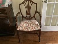 Front view of captain dining chair showing shield back with carved vertical splats and original floral brocade seat upholstery with floral pattern in orange, cream, and brown tones.
