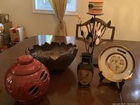 Wide view of all five items on table – jagged bowl, ceramic jar with cutouts and lid, metal leaf candle holder, Chokin plate, small vase