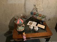 View of the full collection of items on a wooden table including the glass bowl, string lights, jewelry holder, china jars, picture frames, and musical carousel