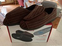 Pair of brown striped men's slippers on top of the product box, showing the exterior and overall design.