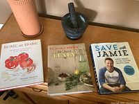 Photo of three cookbooks and black marble mortar and pestle on a wooden surface next to the terra cotta wine cooler.