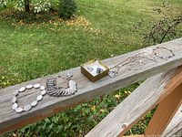 All jewelry pieces including bracelets, pendant with chain, and rings arranged outdoors on wood railing.