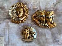 Three Venetian ceramic carnival masks with gold and silver finishes, shown together on a fabric background.