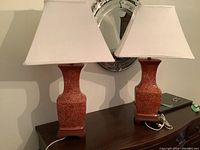Two vintage rust-colored ceramic table lamps with delicate cream floral etching, on wooden bases with cream tapered square shades and rust finials on top