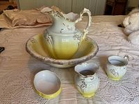 Overall view of the vintage washbowl set including washbowl, pitcher, soap dish, vase, and mug. Set is yellow to white gradient with gold details.