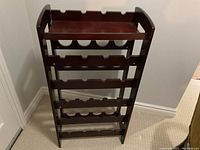 Full front view of the wooden wine rack showing 5 rows of horizontal bottle holders and hinged shelf on top.