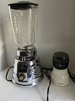 Osterizer Deluxe Blender with glass container attached and Moulinex grinder next to it, both plugged in.