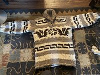 Full view of hand-knitted child's Cowichan style pullover sweater laid flat, showing overall design, pattern and collar detail.