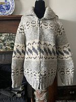 Front view of Cowichan style wool knit sweater on black mannequin showing chunky knit texture, pattern bands in brown and cream, shawl collar, and full front zipper.