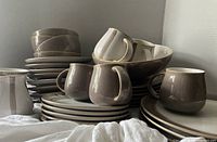 Wide view of stacked and grouped Denby Truffle and Truffle Layers dinnerware including plates, bowls, and cups showing beige and brown glazes.