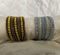 Both bracelets displayed side by side on beige fabric, showing their layered wrap style and bead details.