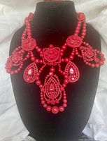 Front view of red enamel bib necklace with detailed bead and cutout design on a black bust display.