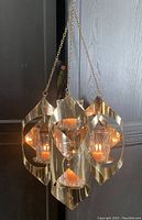 Brass hanging candelabra lit with candles, showing its design and size approximately 11 inches high and 12 inches across with 12-inch chains.