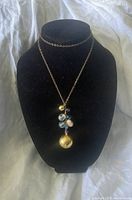 Full view of gold-tone necklace with attached pendant and decorative beads displayed on black bust.