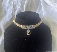 Three strand pink faux pearl choker on black jewelry stand showing rhinestone centerpiece with dangling pendant