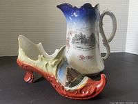 Photo showing blue ceramic jug with curled handle and cherry blossom decoration alongside ornate ceramic shoe figurine with curled heel and colorful paint.