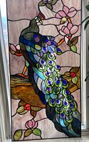 Front view of stained glass panel depicting a colorful peacock on a branch with pink flowers.
